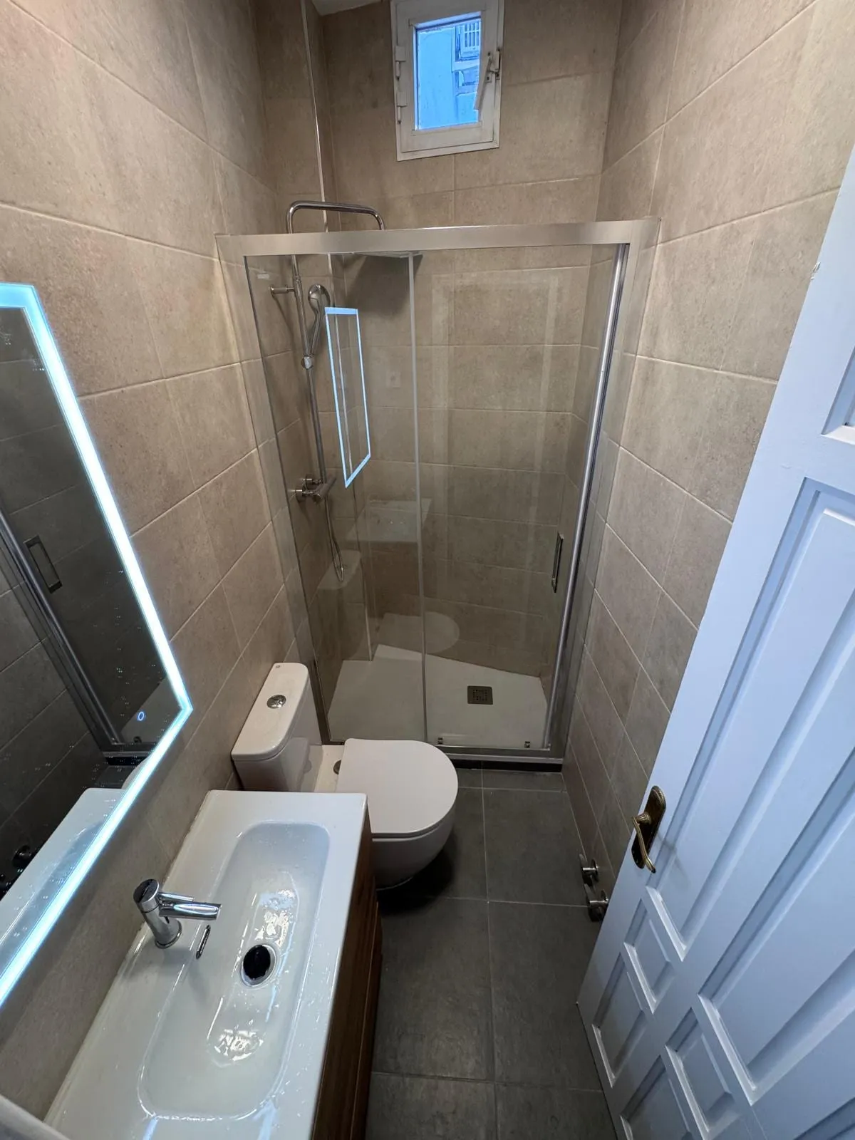 Baño nuevo con mampara de cristal, lavabo con mueble y espejo iluminado